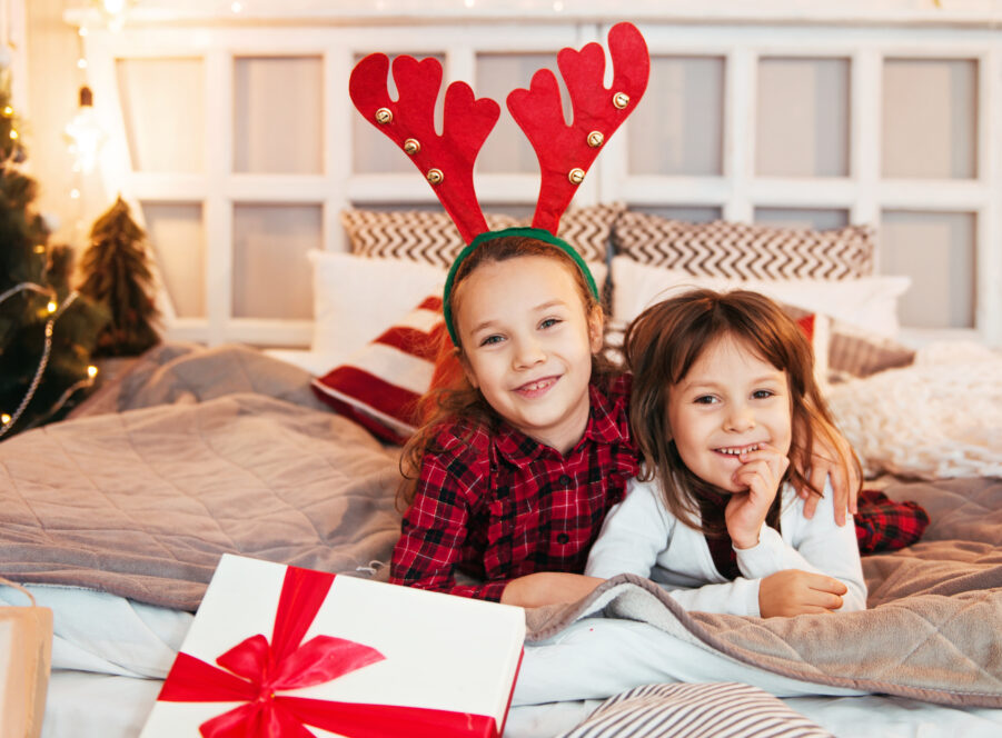 Two cute girls with Christmas presents, playing on the bed