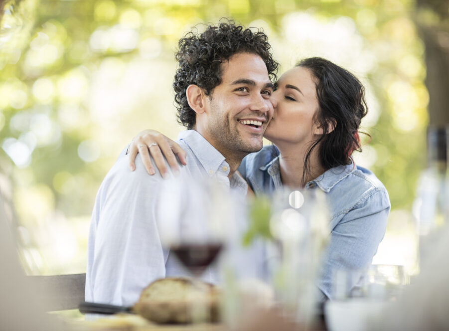 Young woman kissing a happy young man at outdoor table