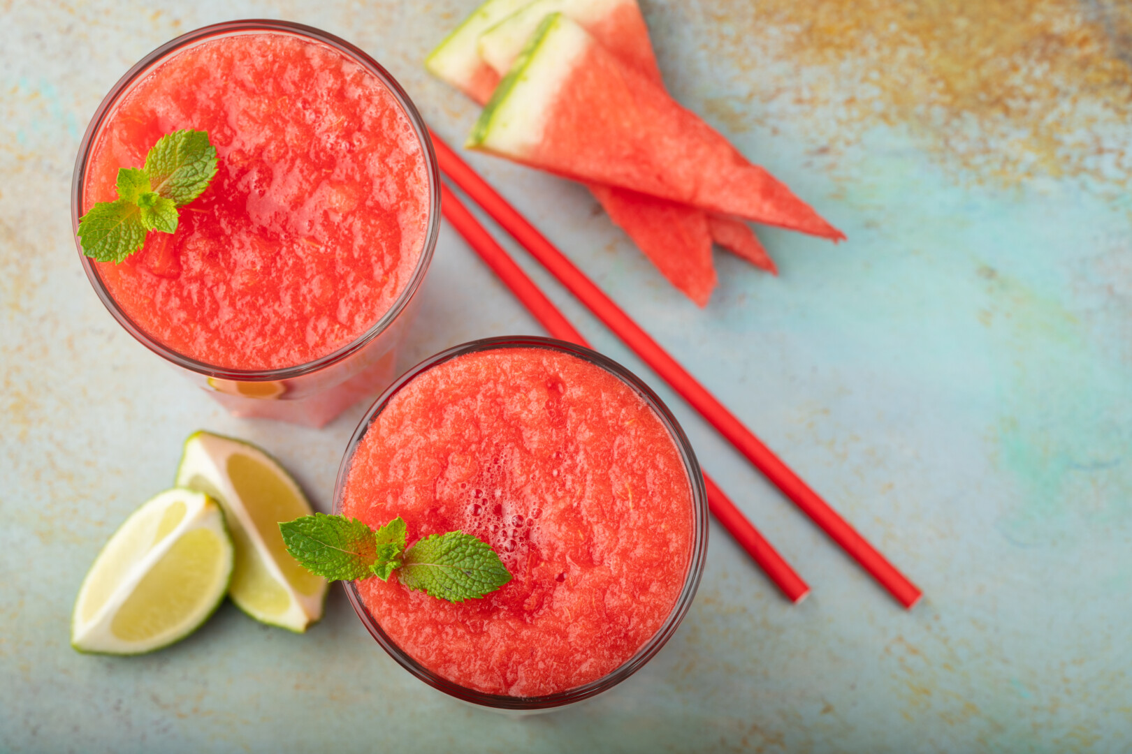 Watermelon slushie with lime, summer refreshing drink in tall glasses on a blue rusty background. Top view with copy space.