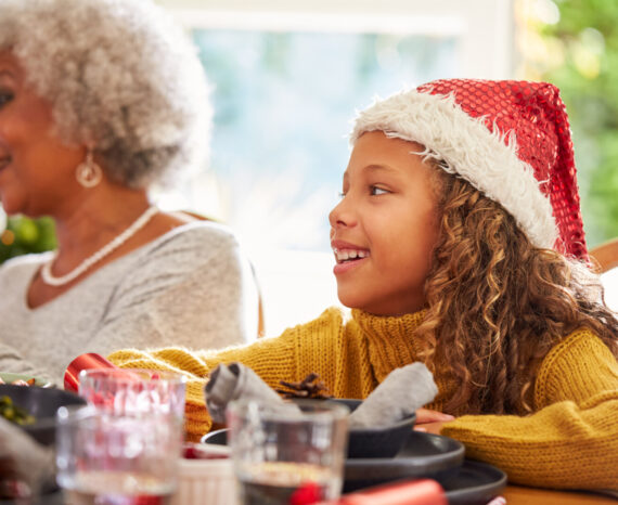 Granddaughter And Grandmother At Dining Table Enjoying Christmas Meal At Home Together