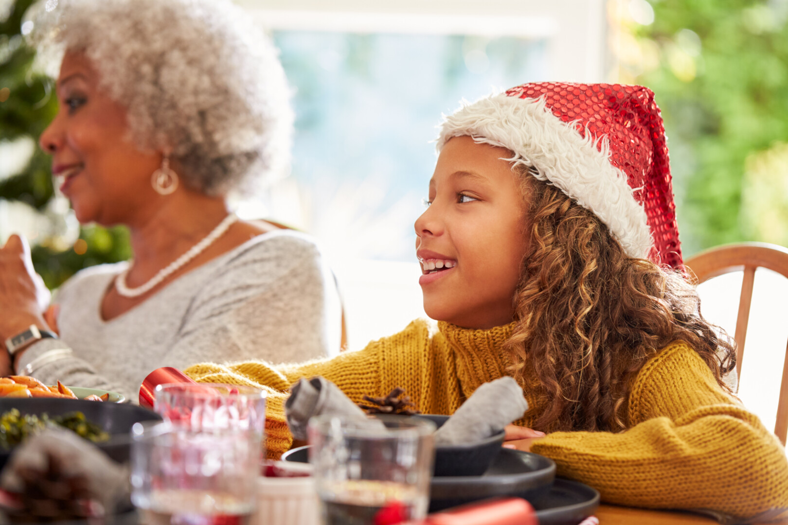 Granddaughter And Grandmother At Dining Table Enjoying Christmas Meal At Home Together